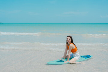 Fototapeta premium Young woman with surfboard looking away while standing against sea during sunset. Happy young woman heading into the surf carrying long board.