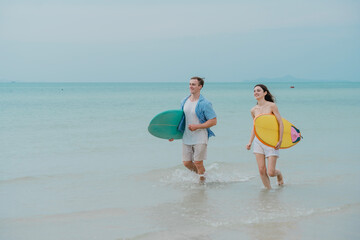 Happy young couple with surfboards enjoying a tropical beach holiday by the turquoise sea on a paradise island. capturing the lifestyle of happy people on a relaxing holiday by the ocean. baech.