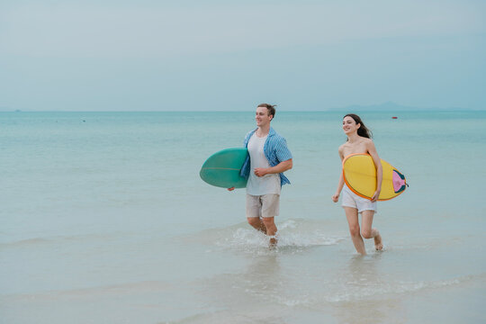 Happy young couple with surfboards enjoying a tropical beach holiday by the turquoise sea on a paradise island. capturing the lifestyle of happy people on a relaxing holiday by the ocean. baech.