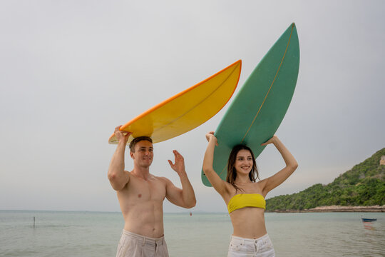 Happy young couple with surfboards enjoying a tropical beach holiday by the turquoise sea on a paradise island. capturing the lifestyle of happy people on a relaxing holiday by the ocean. baech.