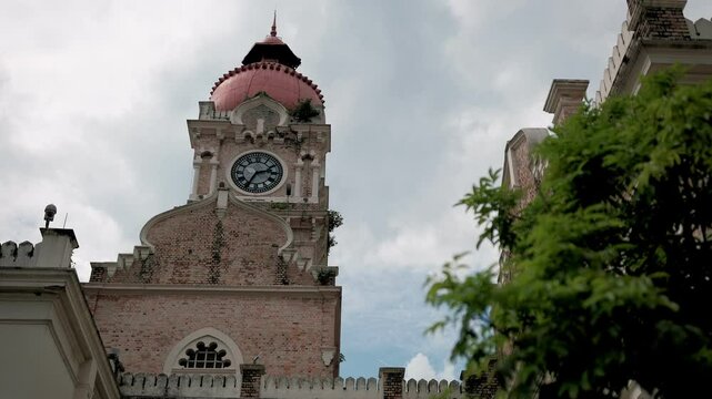 Sultan abdul samad building's iconic pink clock tower rising above lush foliage in historic kuala lumpur cityscape, partially hidden by verdant greenery