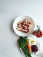 Ingredients for traditional borscht on plates – vegetables, pork ribs, and tomato sauce, isolated on white background