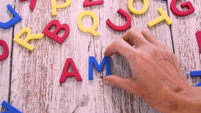 A female hand writing the word amor with colorful foam letters on a wooden background. High angle view and Spanish language.