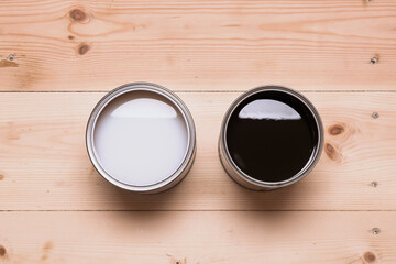 Two open cans with different wood coatings, light and dark, stand side by side on wooden floor,...