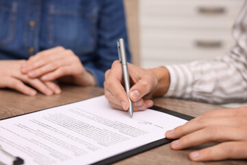 Man putting signature on document at table, closeup
