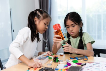 Fototapeta premium Two young girls are engaged in a STEM activity, building and exploring with colorful robotics kits at a table, fostering hands-on learning.