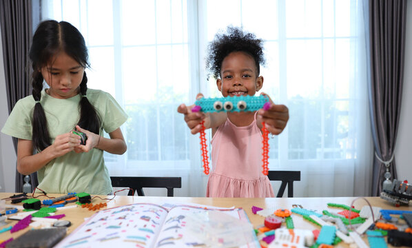 Two young girls, one Asian and one African-American, enjoy a STEM activity, building and learning with colorful construction toys and robotics parts at a bright table.