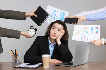 Woman overwhelmed by different requests from colleagues at desk against gray background