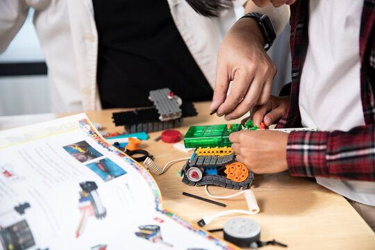 Close-up of a person's hands diligently assembling a colorful robot from construction blocks, guided by an open instruction manual.