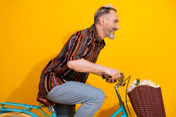 Smiling mature man rides a decorative bicycle with flowers in front of a yellow background wearing...