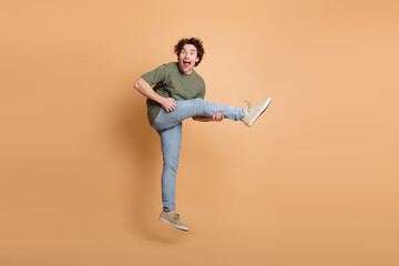 Cheerful curly haired man in casual khaki shirt and jeans posing energetically against a beige...