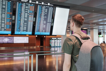 A young male traveler checks the airport departure board wearing a backpack. Concept of travel...