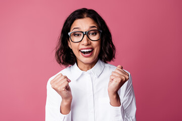 Young woman in white shirt with glasses expressing joy and delight against a pink background