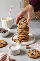Woman taking homemade brown butter chocolate chip cookies with salt from plate on table. Selective focus.