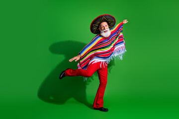 Energetic mature man dressed in vibrant traditional Mexican attire dancing on a green background with a sombrero and poncho.