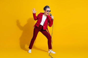 Mature woman in a stylish red outfit singing passionately with a microphone on a vivid yellow background