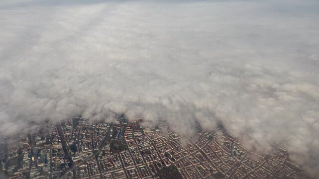 Aerial view of Munich, Germany, with the city partially covered by thick clouds and fog, revealing detailed urban patterns and the Olympic Tower piercing the cloud layer