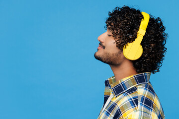 Close up side view young happy Indian man wear yellow checkered shirt casual clothes listen to...