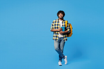 Full body young happy smiling smart Indian boy student he wear yellow casual clothes backpack bag hold books looking camera isolated on plain blue background. High school university college concept.
