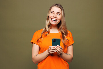 Young smiling woman she wears orange t-shirt casual clothes hold in hand use mobile cell phone look...