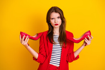 Adorable woman holding red high heels against a yellow background, wearing a stylish red suit and...