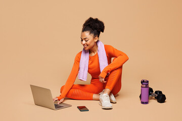 Full body young fitness trainer instructor woman wear orange clothes towel spend time in gym sit...