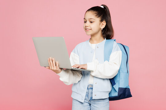Young school IT girl 8-9 years old wear blue casual clothes backpack hold use laptop pc computer chatting online isolated on plain pink background children portrait. Childhood kids education concept.