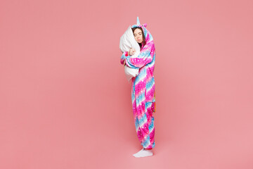 Full body young calm sleepy woman wearing domestic costume with hoody hold pillow under head close...