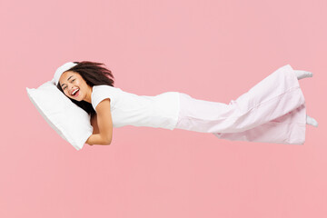 Naklejka na ściany i meble Full body side view calm young woman wearing pyjamas jam sleep eye mask rest relax at home fly fall hover over air hurry up hold pillow isolated on plain pink background. Good mood night nap concept.