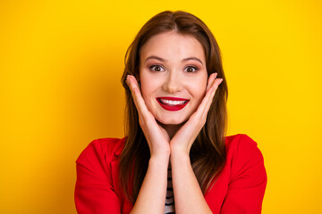 Adorable woman in a vibrant red jacket expressing surprise and joy against a vivid yellow...