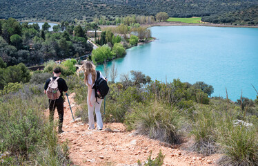 Young hikers walking downhill along trail near turquoise lake in natural setting

