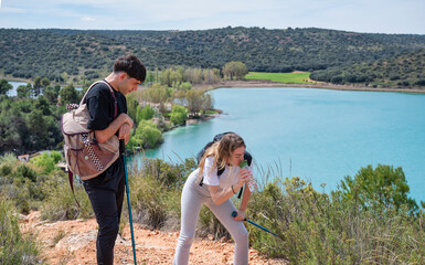 Young hikers pausing on trail, girl bent over drinking water while boy watches, standing with...