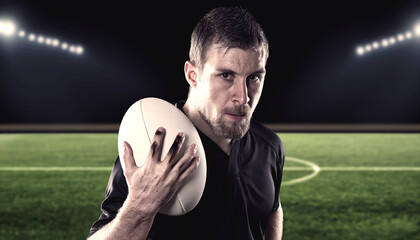 Rugby player in black kit intensely holding a rugby ball under stadium floodlights.