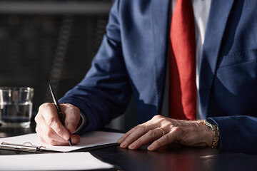 Close up on hands of Caucasian middle aged businessman wearing suit and wristwatch signing document with pen at desk in modern office