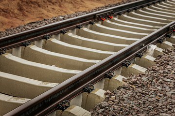 Detailed view of rusted steel railway tracks mounted on white concrete sleepers, captured at a...