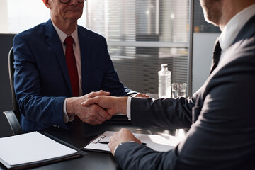 Over shoulder shot of senior Caucasian man in suit shaking hands with male colleague making...