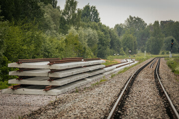 Long, straight railway tracks stretch into the distance between green forest areas under a cloudy...