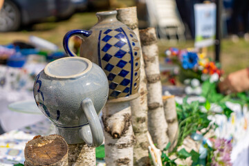 Folk-style ceramic jugs with decorative patterns displayed on birch logs at a craft fair stall....