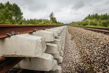 Layered concrete railway track sections are stacked beside an active rail line, viewed from the...
