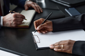 Close up on hands of Black businesswoman writing on clipboard during business meeting with Caucasian middle aged male colleague at office