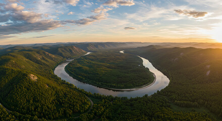 A wide aerial view of a winding river cutting through green forest.