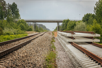 A close side view of stacked concrete railway track sections alongside a railway line, with a...