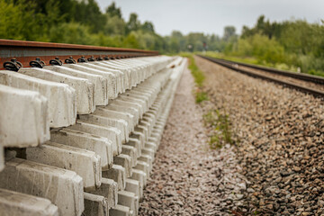 Layered concrete railway track sections are stacked beside an active rail line, viewed from the...