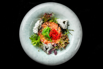 A gourmet salmon tartare dish, garnished with seaweed and mixed greens, elegantly plated with...