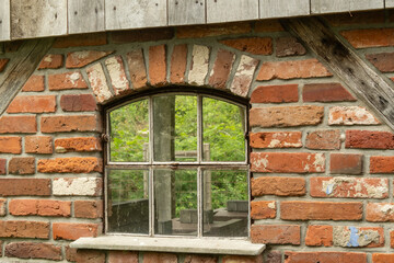 Arched window reflecting greenery in old brick wall building