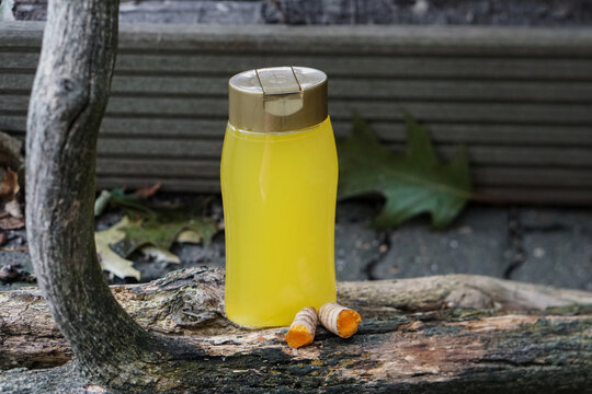 DIY homemade turmeric face toner in a transparent bottle, displayed with fresh turmeric root on dark textured tree bark. Natural skincare and organic beauty.      