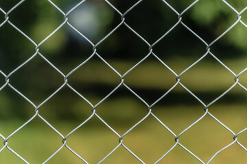Close-up of metal chain link fence with blurred green background.