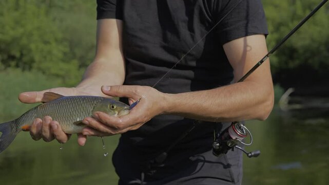 A fisherman with a catch in his hands stands on the river bank. In his hands is a Chub fish