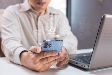 A person updates a smartphone while sitting at a desk with a laptop, illustrating technology use and connectivity.