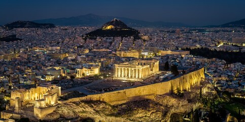 Aerial closeup up of the illuminated Parthenon Temple at the Acropolis of Athens, Greece, with the skyline of the city behind